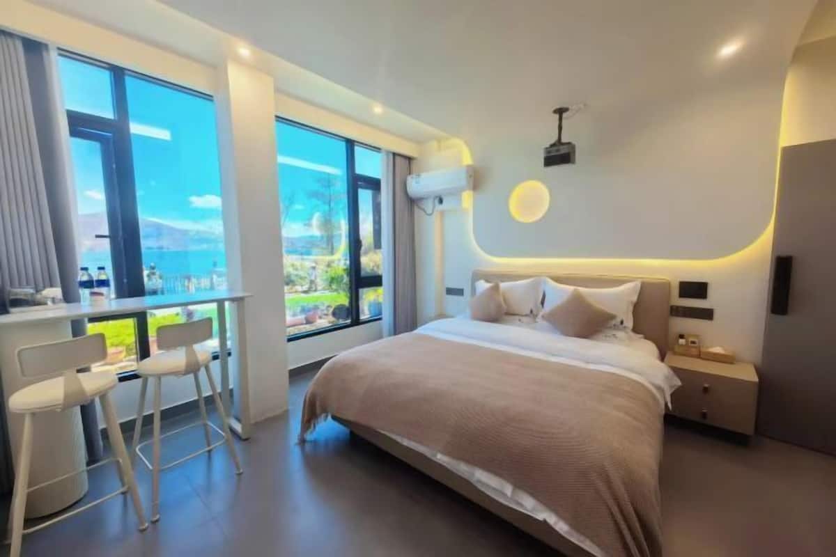 A modern bedroom with a large bed, a desk with two chairs, and a view of the outdoors.
