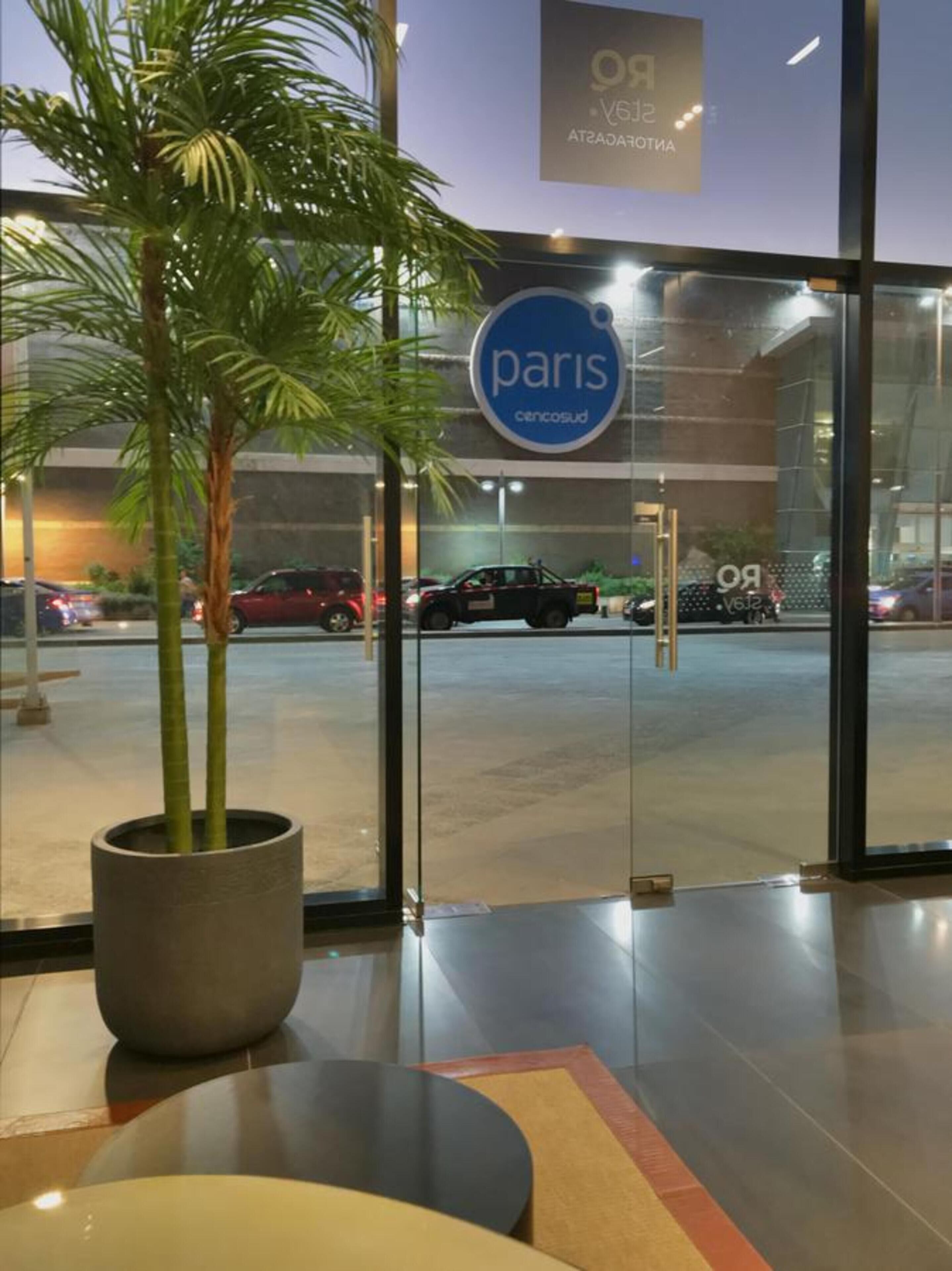 A modern building entrance with a large glass door, a sign reading "paris", and a potted plant in the foreground.