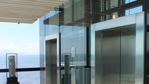 Un área de ascensores moderna con paredes de vidrio y vista al océano.