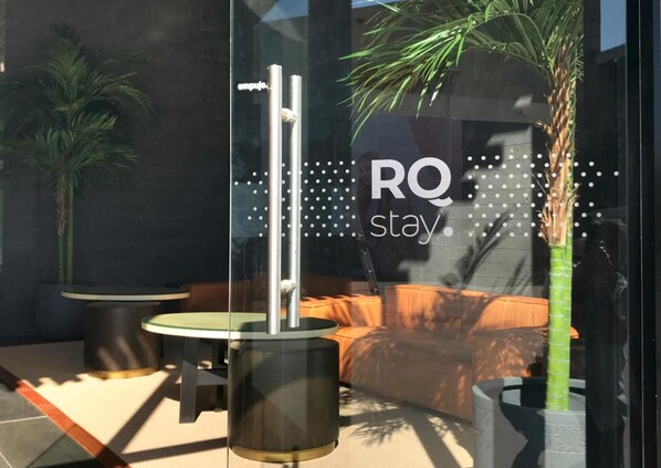 A modern outdoor seating area with a glass partition, a metal pole, and a sofa.