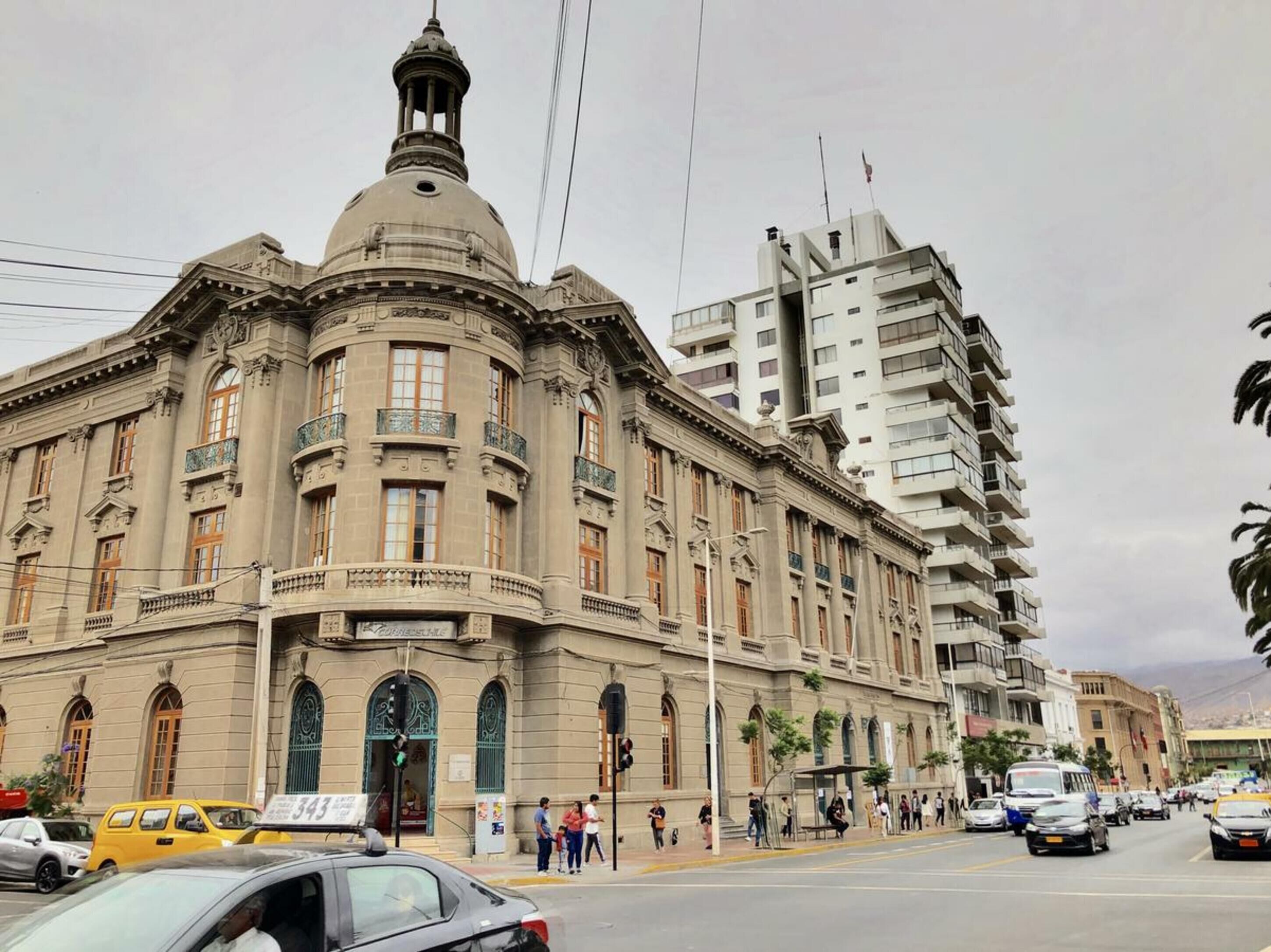 Un bâtiment historique doté d’un dôme imposant et d’une architecture classique, situé dans une rue animée, à proximité d’immeubles modernes.