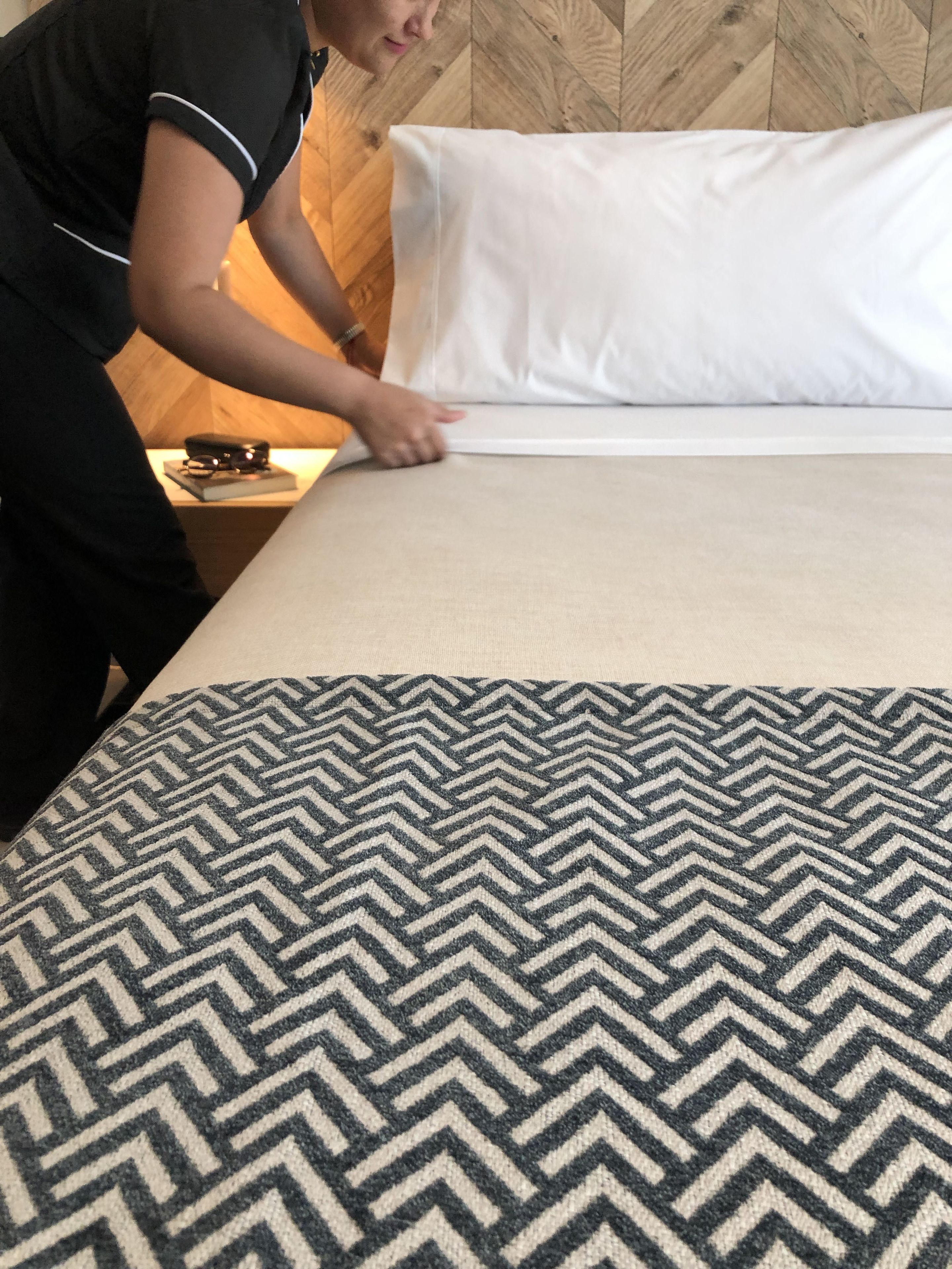 Een bed met een bedsprei met patroon, een wit kussen en een houten hoofdbord.