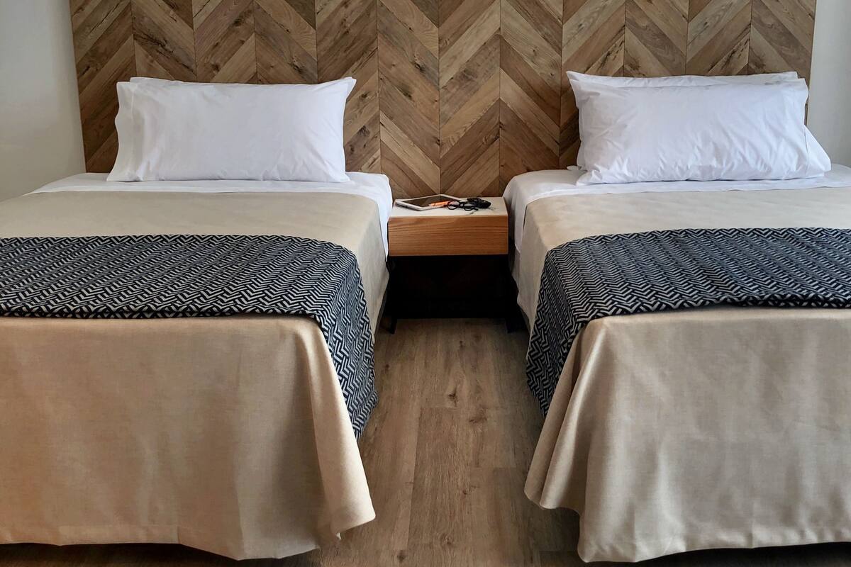 Una habitación de hotel con dos camas, un cabecero de madera con diseño espiga y suelo de madera.