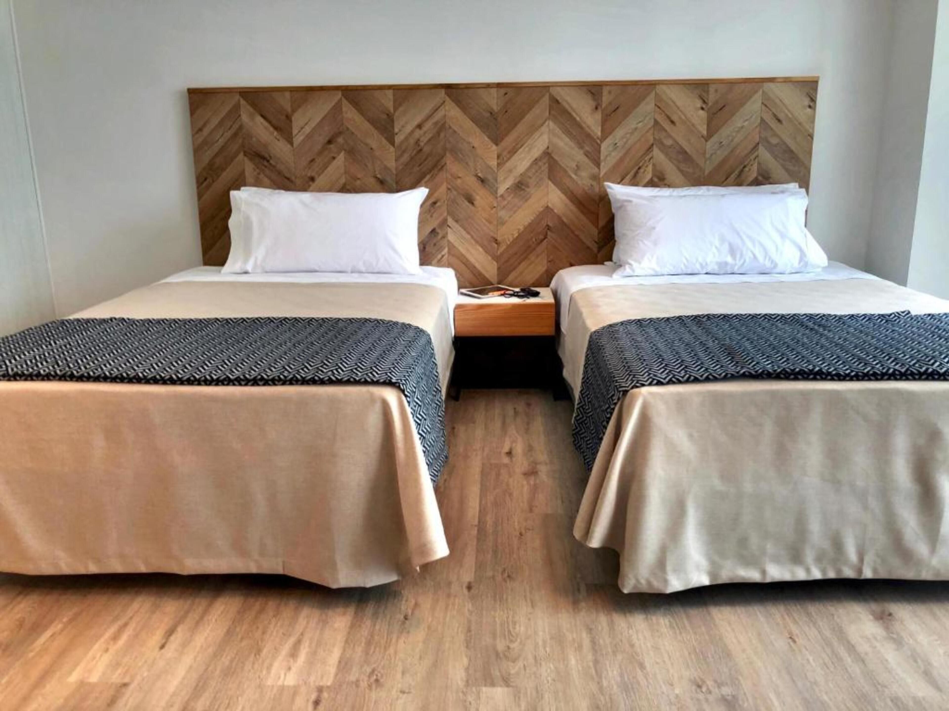 Quarto duplo com duas camas, cada uma com cabeceira de madeira e colcha estampada.