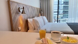 Una habitación de hotel con una cama, una mesa de desayuno con un plato de comida, una taza de café y un vaso de jugo de naranja.
