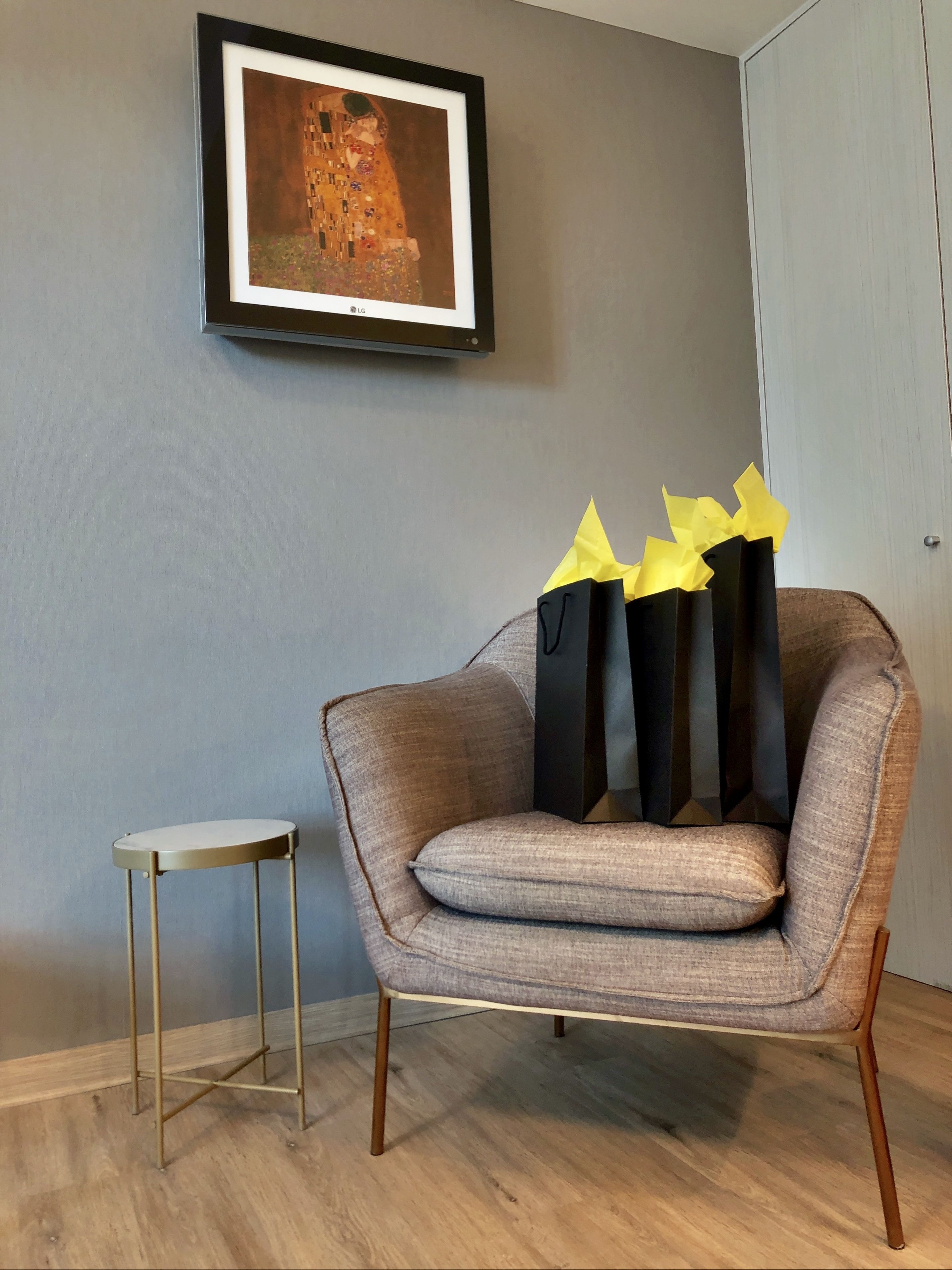A modern room with a grey wall, a framed artwork, a grey armchair, and a small round table.