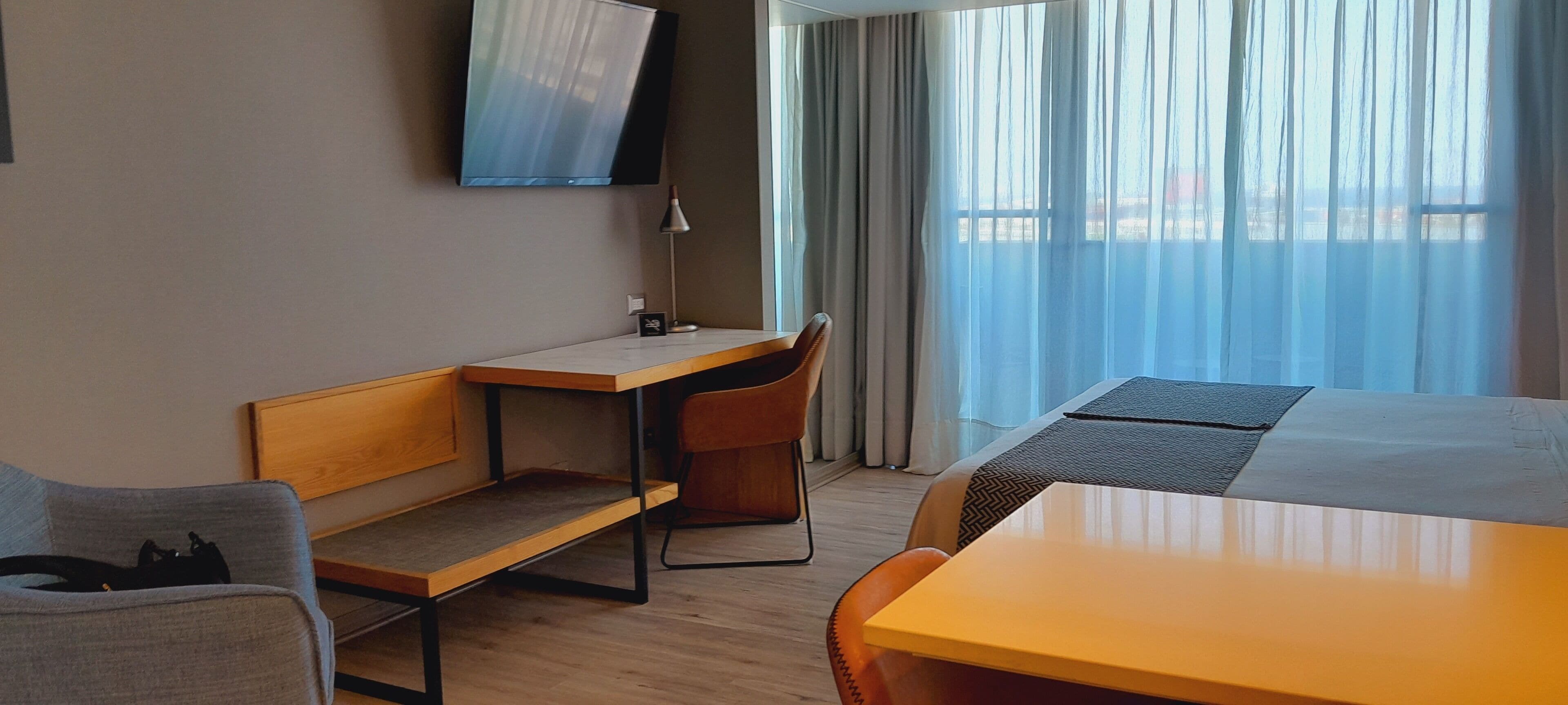 A hotel room with a bed, a desk, a chair, and a TV mounted on the wall.