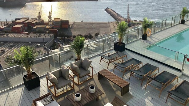 Una terraza en la azotea con piscina, zonas de estar y vistas al mar y al puerto.