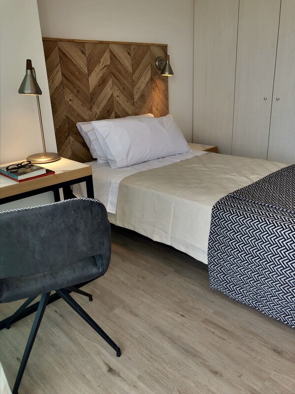 A neatly arranged bedroom with a bed, bedside lamps, a desk with a chair, and a wardrobe.