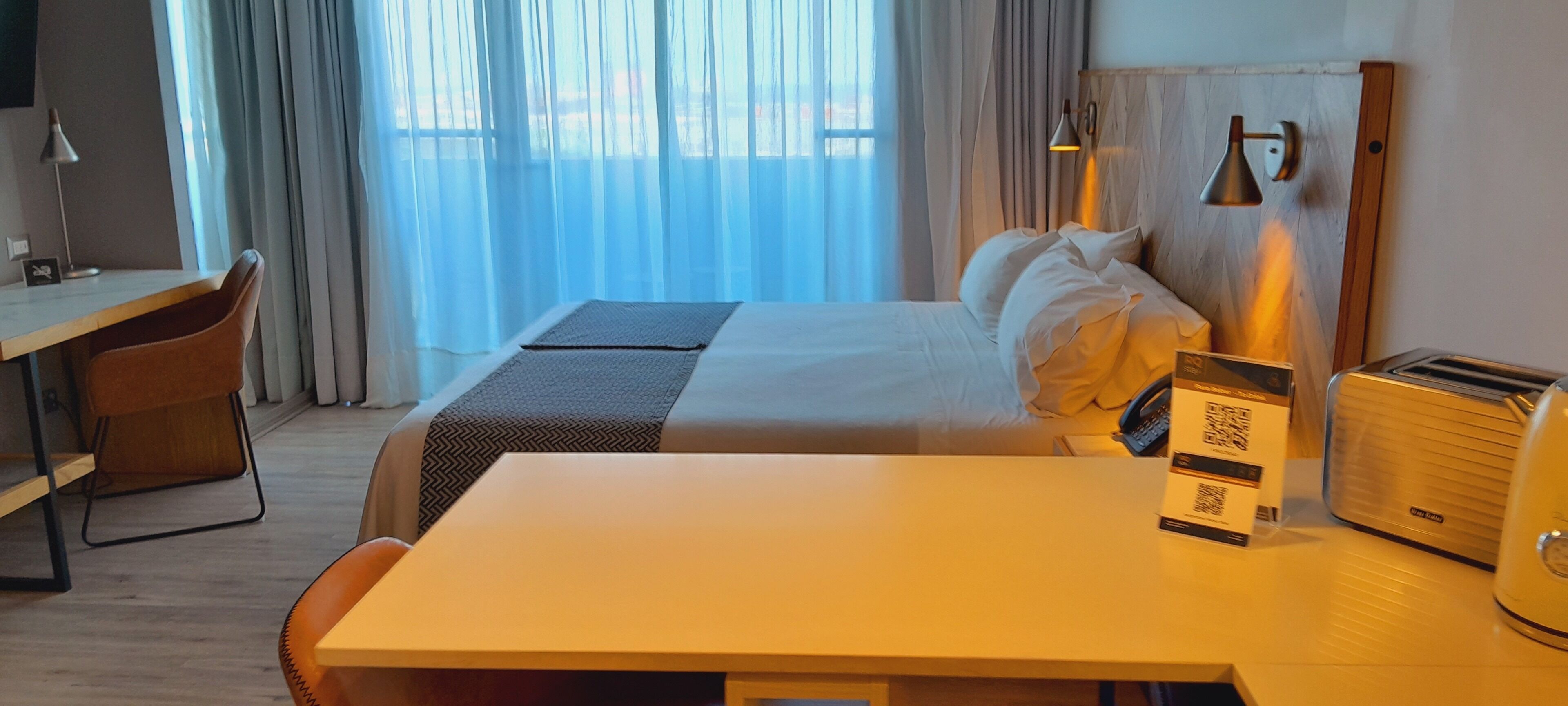 Une chambre d’hôtel équipée d’un lit, d’un bureau, d’une chaise, d’une table, d’une lampe et d’un grille-pain.