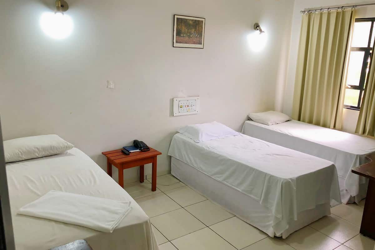 Quarto com duas camas de solteiro, uma pequena mesa de madeira com telefone e livro, uma tomada e um quadro.