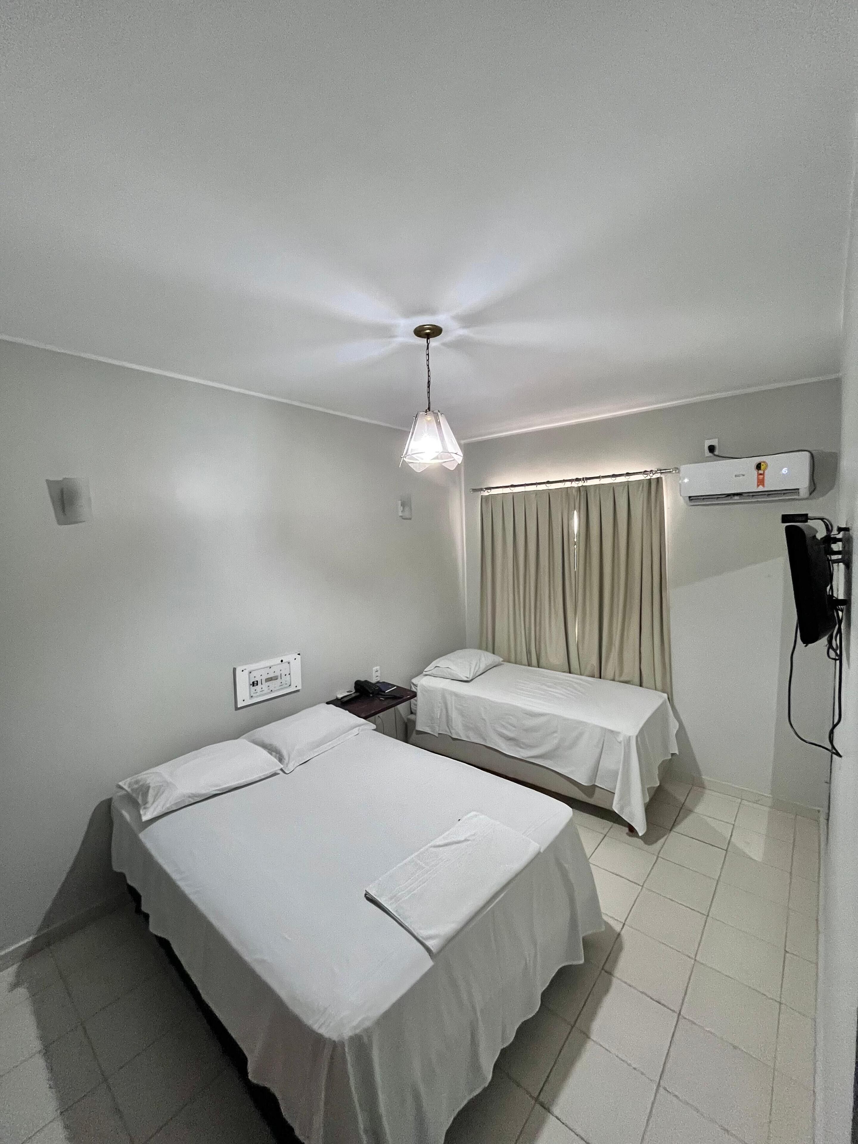 Habitación de hotel con dos camas individuales, ventilador de techo, aire acondicionado y una mesita de noche con lámpara.