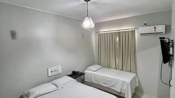 Habitación de hotel con dos camas individuales, ventilador de techo, aire acondicionado y una mesita de noche con lámpara.