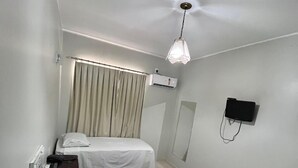 Ein Hotelzimmer mit zwei Betten, einem Deckenventilator, einer Klimaanlage, einem an der Wand montierten Fernseher und einem Vorhang.