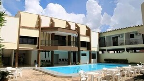 Ein Hotel mit Schwimmbad, Außenbereich zum Sitzen und einem zweistöckigen Gebäude mit Balkonen.