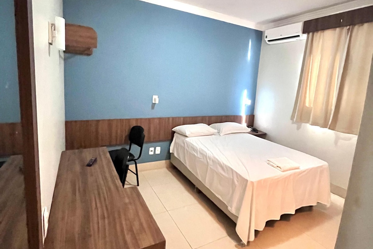 Quarto de hotel com escrivaninha de madeira, uma cama de solteiro e uma cadeira.