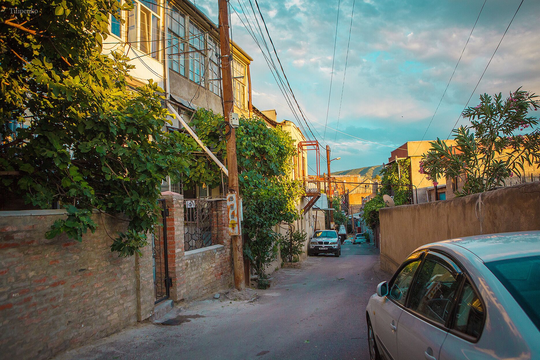 A narrow street with buildings on both sides, a parked car, and overhead power lines.