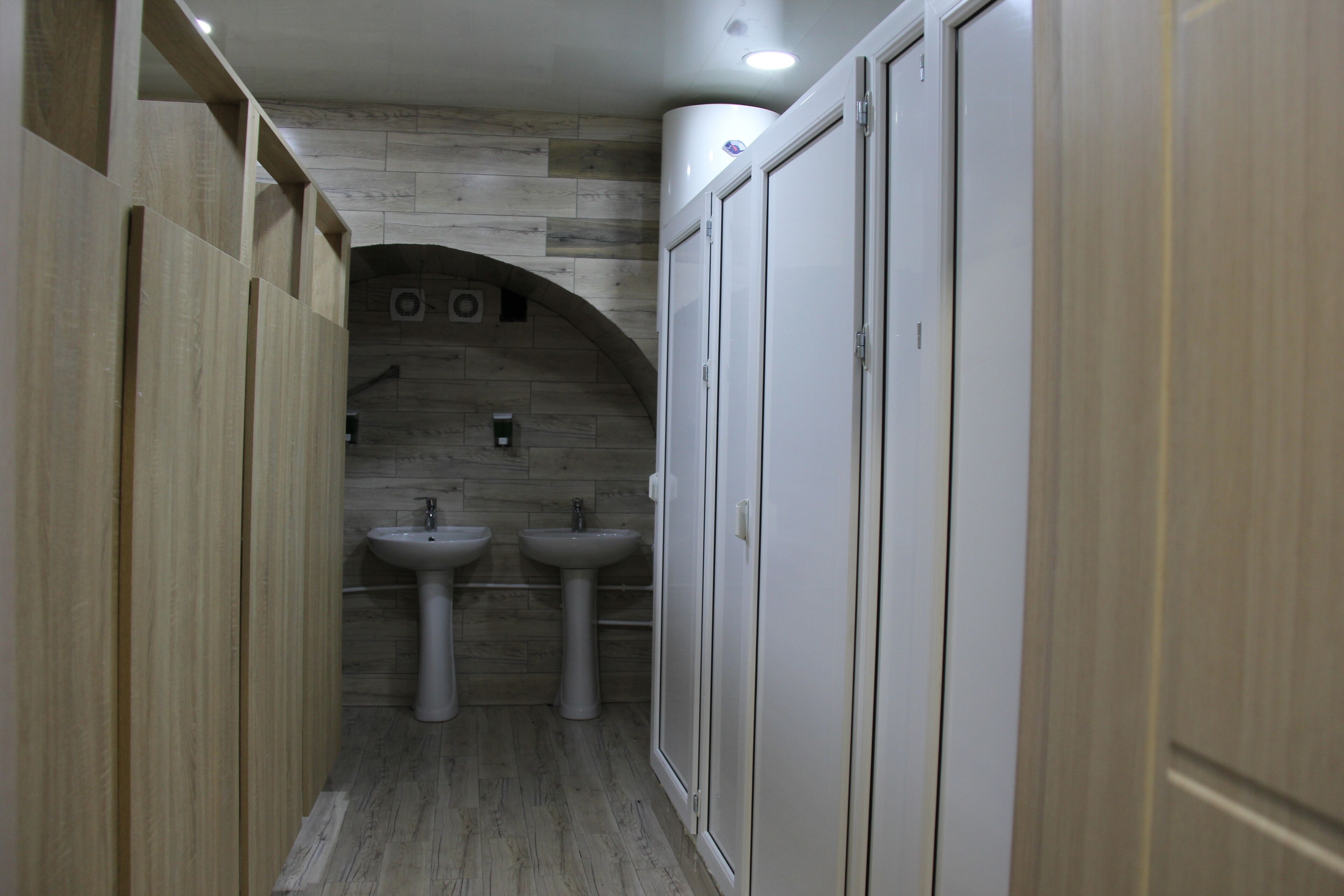 A narrow bathroom with wooden walls, two sinks, and a curved ceiling.