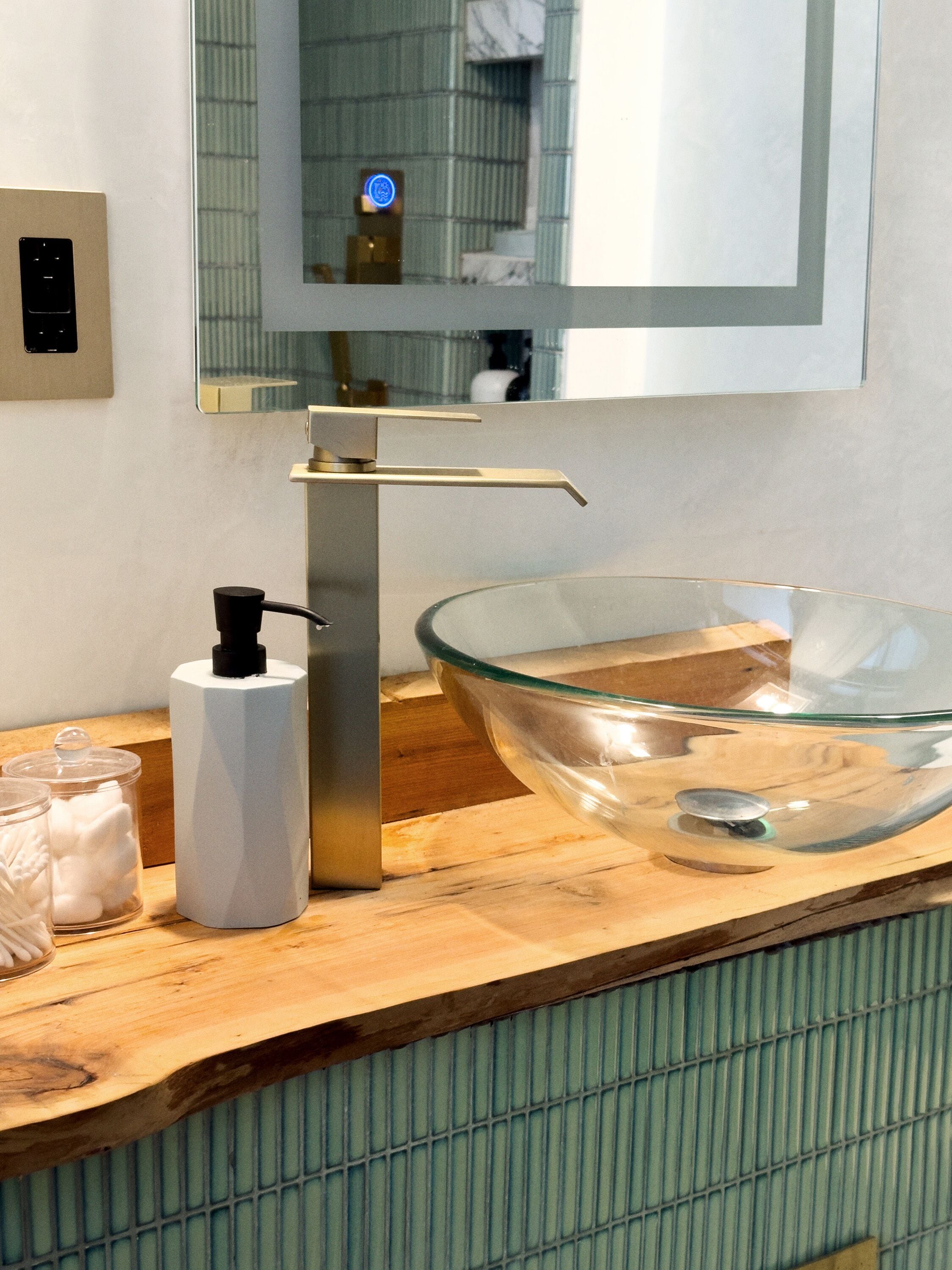 A modern bathroom with a glass bowl sink, a white soap dispenser, and a mirror above the sink.