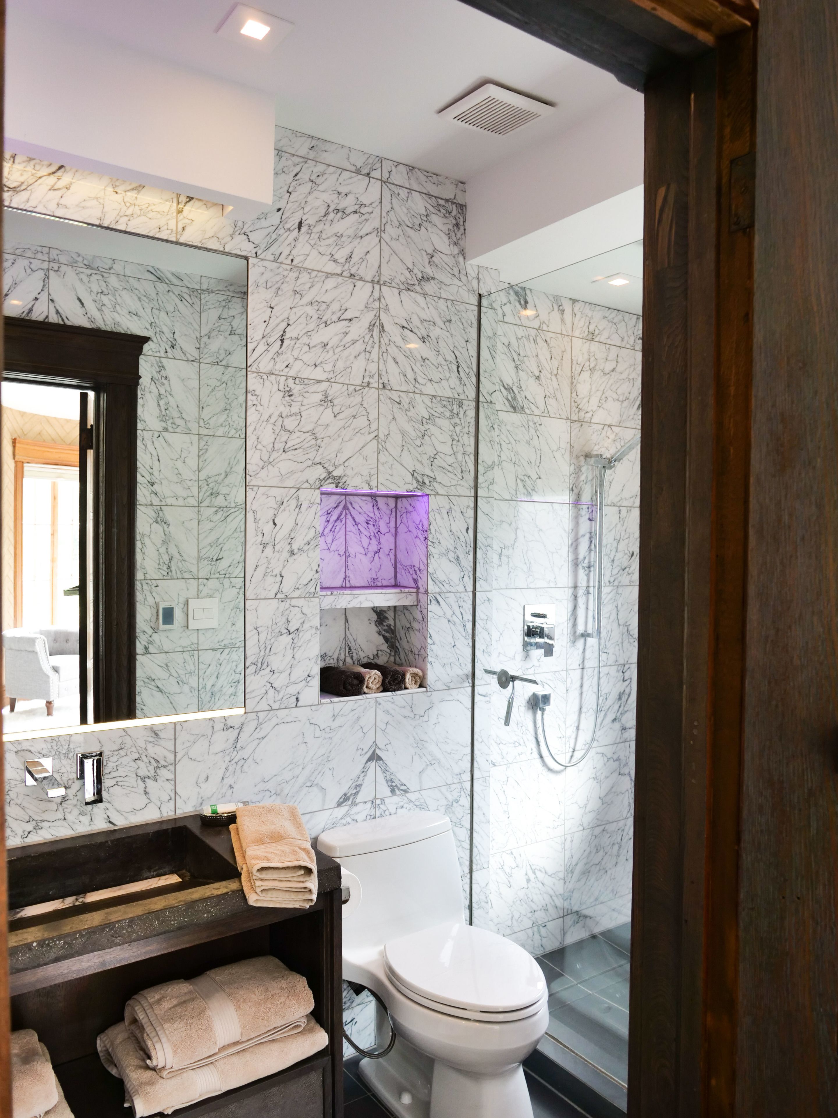 A modern bathroom with a marble backsplash, a vanity with a sink and towel rack, a toilet, and a glass shower enclosure.