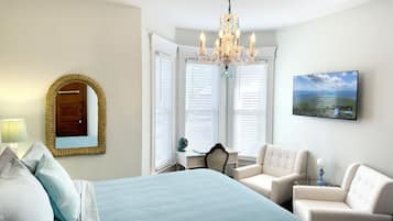 A bedroom with a bed, a chair, a desk, a chandelier, a mirror, and a painting.