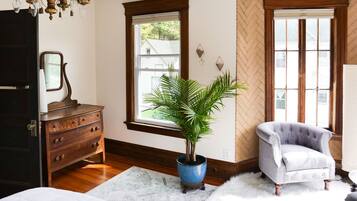 Quarto com cômoda de madeira, planta em vaso, cadeira e lustre.