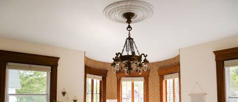 A bedroom with a large bed, a potted plant, two armchairs, a round table, and a chandelier.