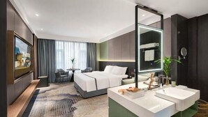 A modern hotel room with a large bed, a separate seating area, a vanity with two sinks, and a large mirror. - Wanxing Hotel (Qu County)