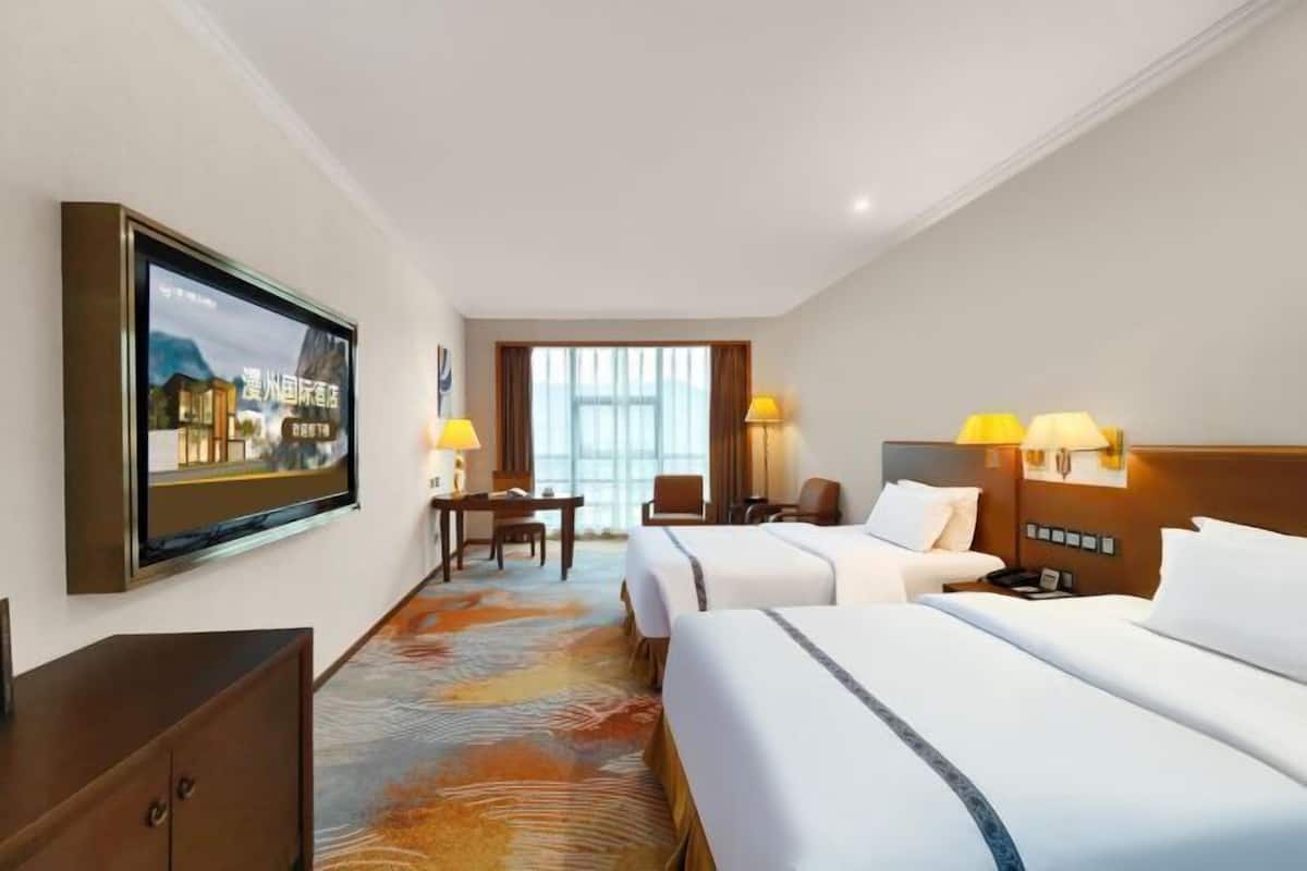 A hotel room with two beds, a desk, and a television mounted on the wall.