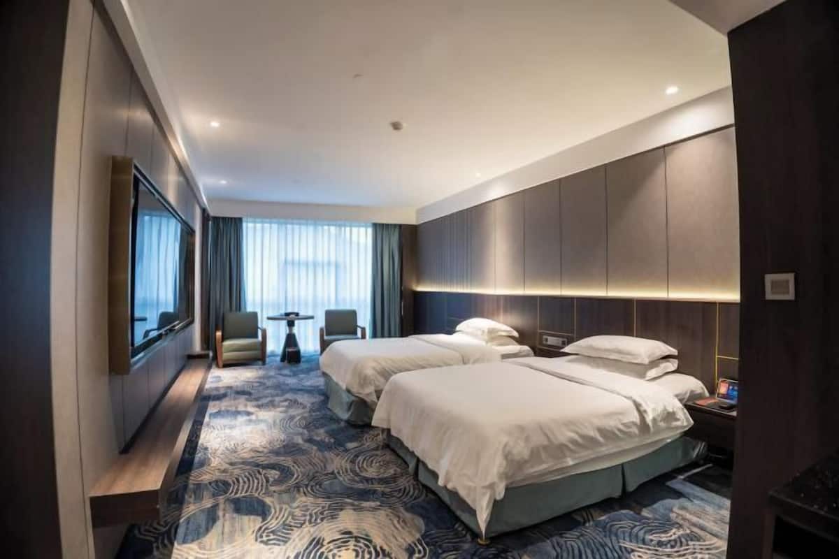A modern hotel room with two beds, a seating area, and a large window.