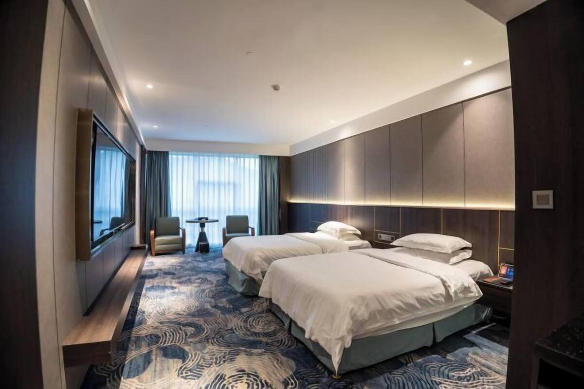 A modern hotel room with two beds, a seating area, and a large window.