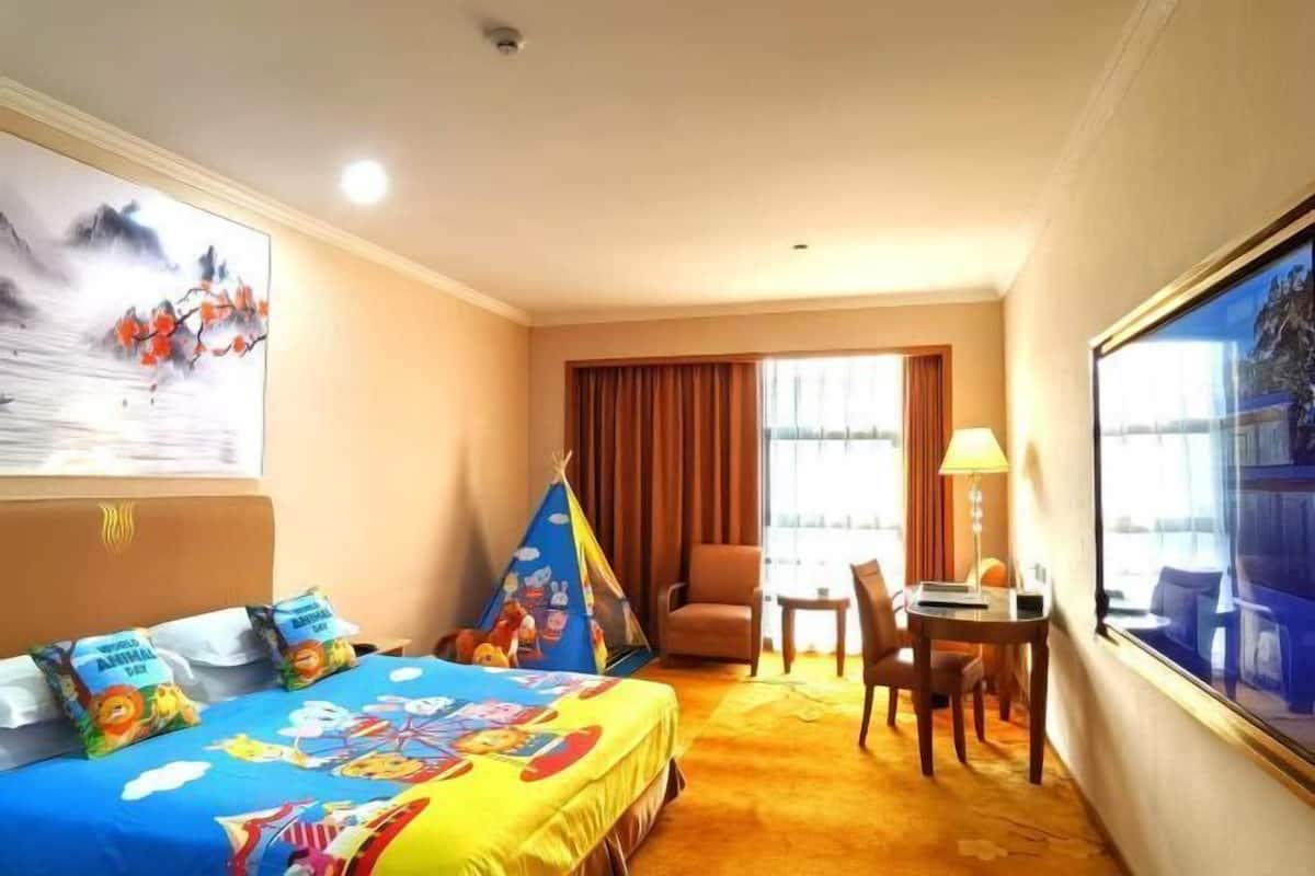 A hotel room with a bed, a chair, a small table, a lamp, and a large window.