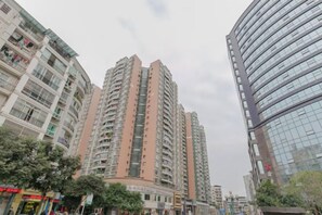 A high-rise residential building with multiple balconies, a curved facade, and a modern glass structure to the right. - Wanxing Hotel (Qu County)