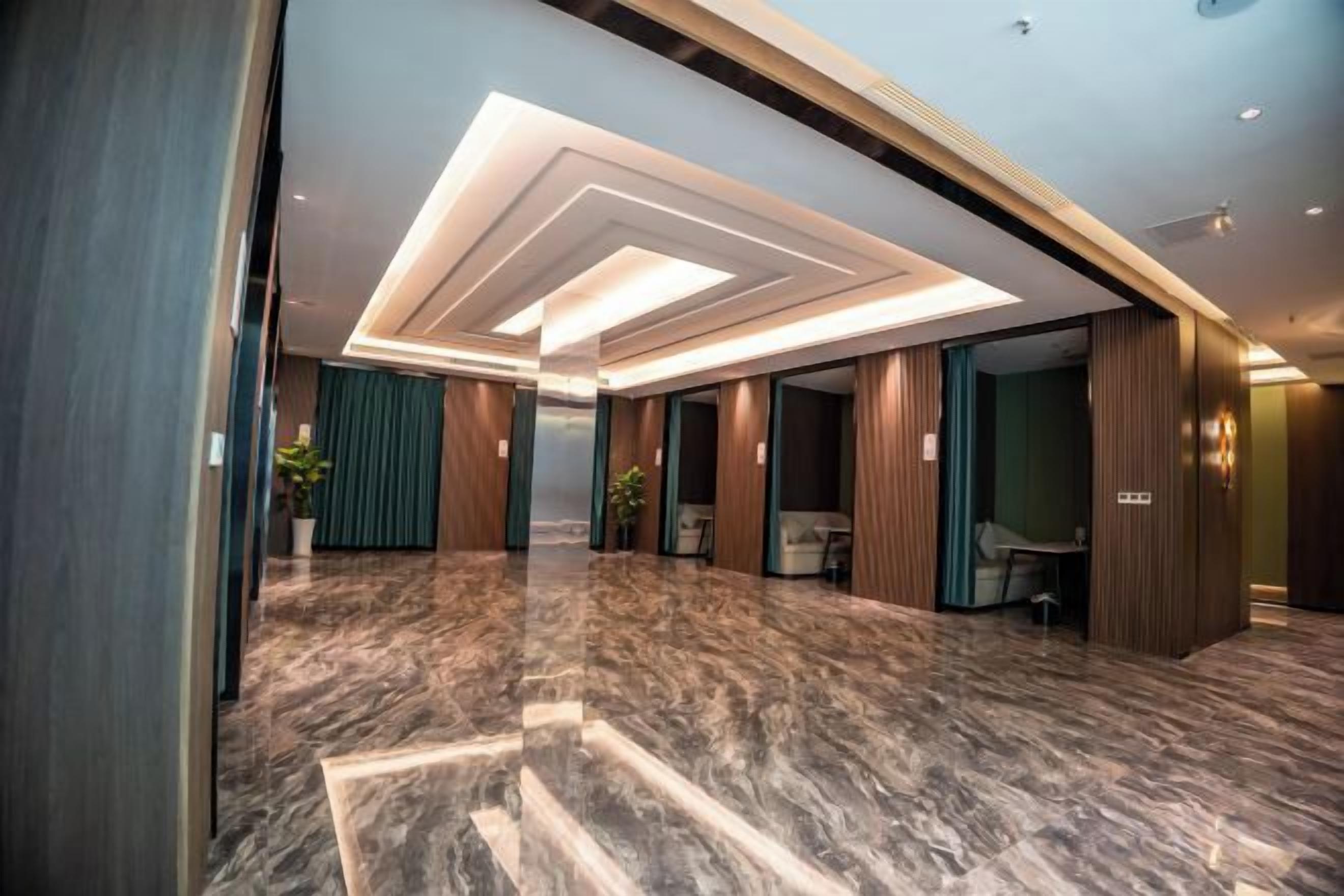 A modern hotel lobby with a marble floor, recessed lighting, and a view into a room with a bed and a desk.
