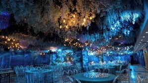 A restaurant with round tables and chairs, a ceiling with hanging lights, and a wall with a waterfall-like design. - Wanxing Hotel (Qu County)