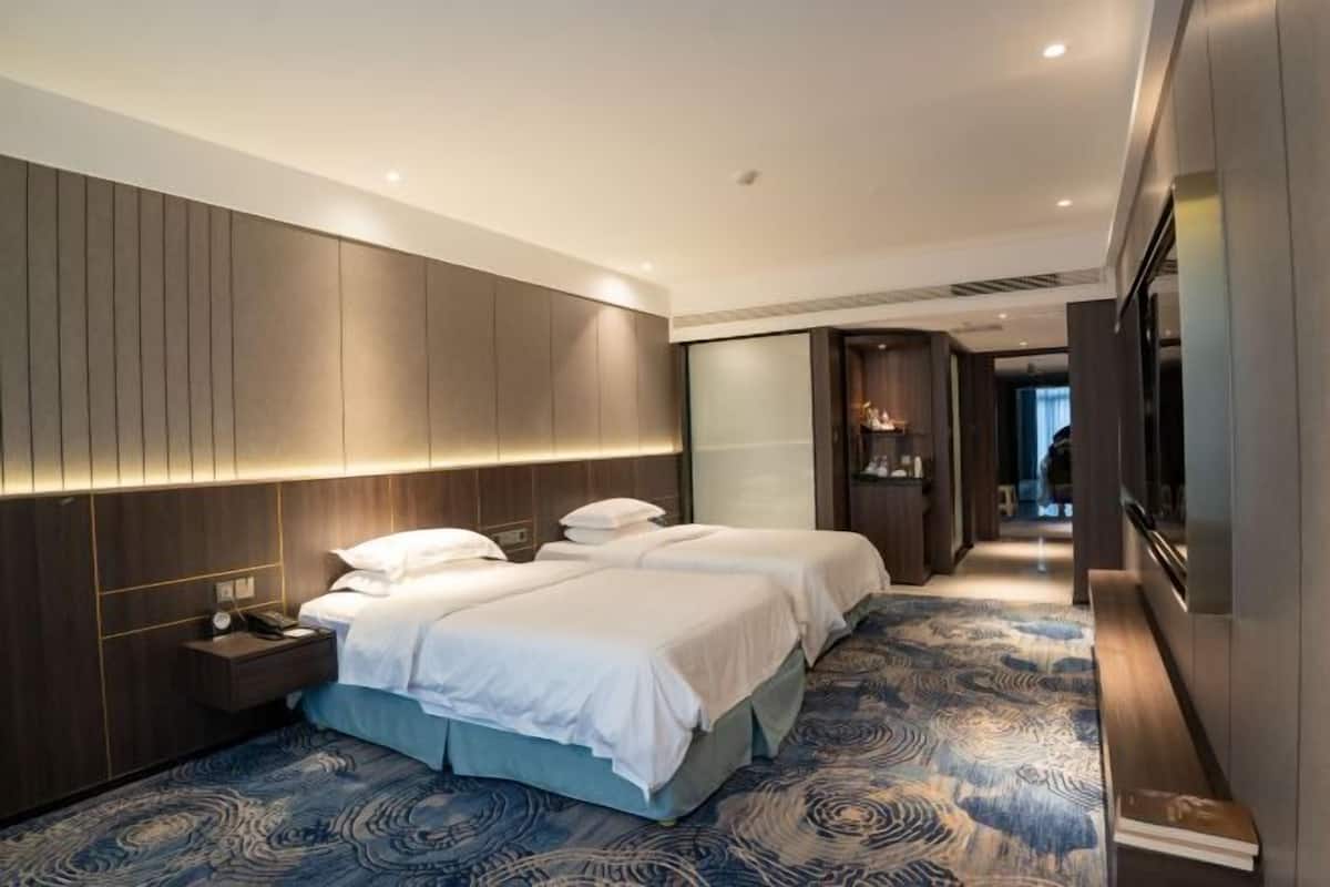 A hotel room with two beds, a nightstand, a large mirror, and a patterned carpet.