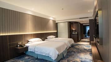 Ein Hotelzimmer mit zwei Betten, einem Nachttisch, einem großen Spiegel und einem gemusterten Teppich.