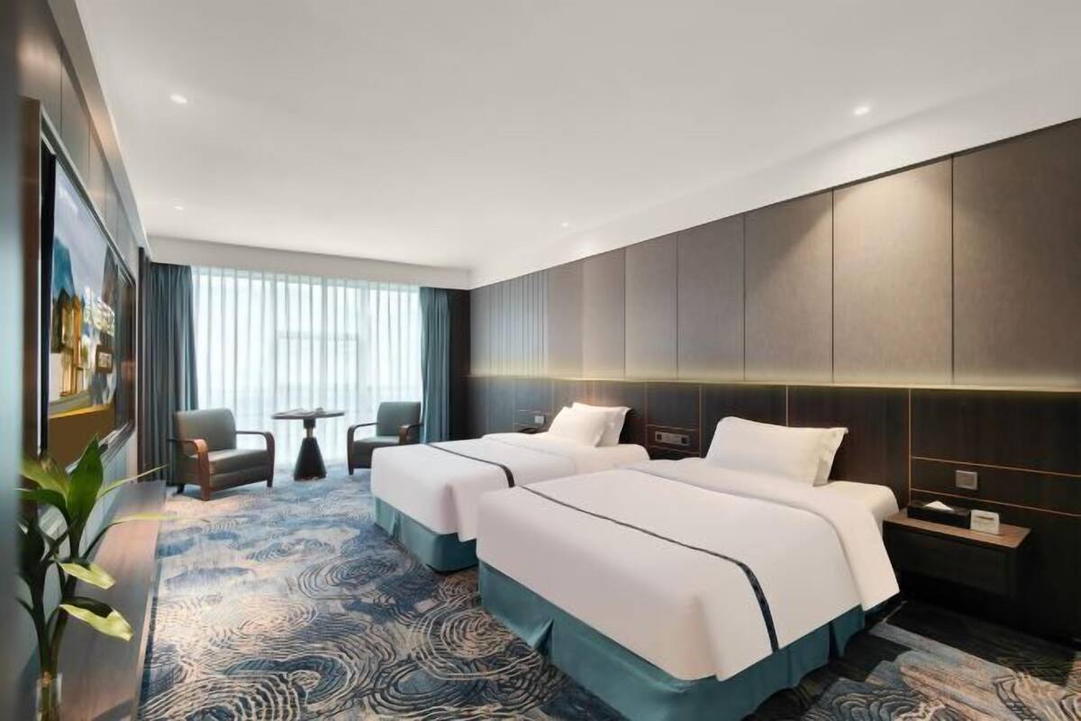 A hotel room with two beds, a small seating area, a large window, and a decorative rug.