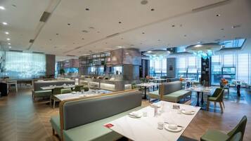 A modern restaurant with multiple dining areas, including booths and tables, and a bar area.