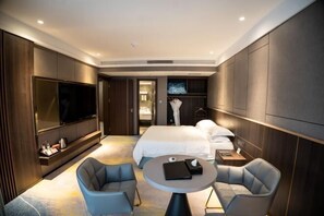 Une chambre d’hôtel moderne dotée d’un grand lit, d’un téléviseur à écran plat fixé au mur, d’une table ronde avec deux chaises et d’une armoire.