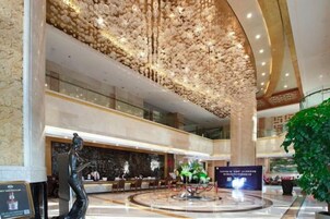 Un vestíbulo espacioso con techo alto, una recepción y un elemento decorativo central.