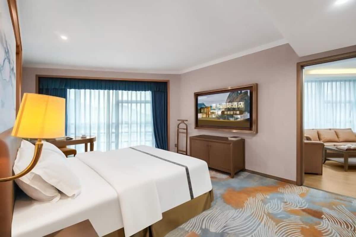 A hotel room with a bed, a desk, a television, and a view of the outside.