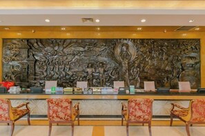 A reception area with a large decorative wall, a reception desk, and four chairs. - Wanxing Hotel (Qu County)