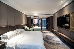 A modern hotel room with a large bed, a seating area, a TV, and a view of the city. - Wanxing Hotel (Qu County)