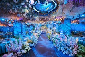 A venue with a central aisle flanked by floral arrangements and lanterns, leading to a stage area. - Wanxing Hotel (Qu County)