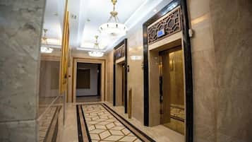 A hallway with marble flooring, chandeliers, and elevators.