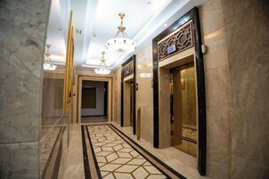 A hallway with marble flooring, chandeliers, and elevators.
