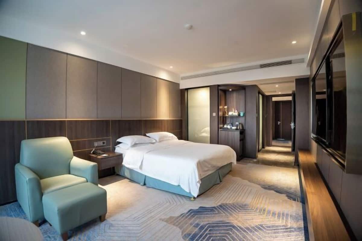 A modern hotel room with a large bed, a seating area, and a walk-in closet.