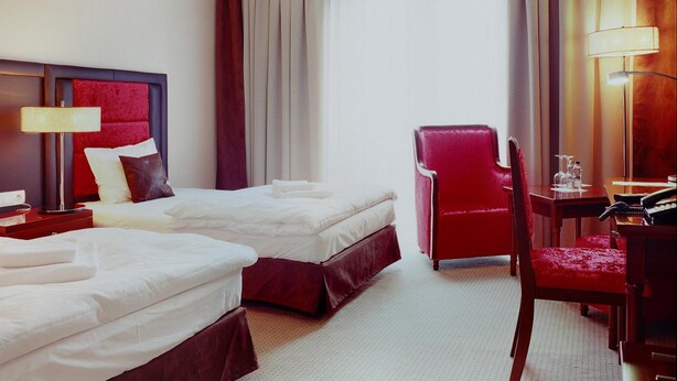 A hotel room with two beds, a desk with a chair, a lamp, and a large window with curtains. - Hotel Alhar (Lubliniec)