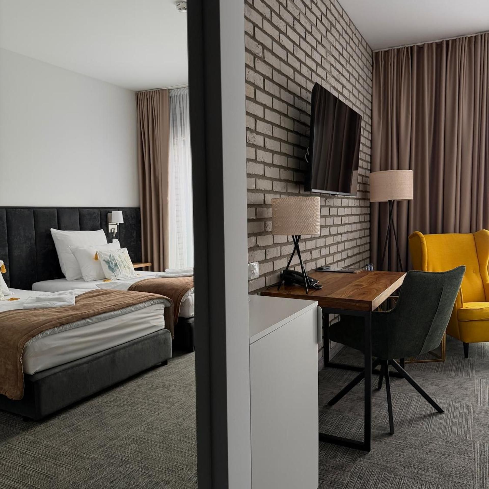 Ein Hotelzimmer mit Backsteinwand, einem Flachbildfernseher, einem Schreibtisch mit Stuhl, einem Bett mit Kopfteil und einem gelben Sessel.